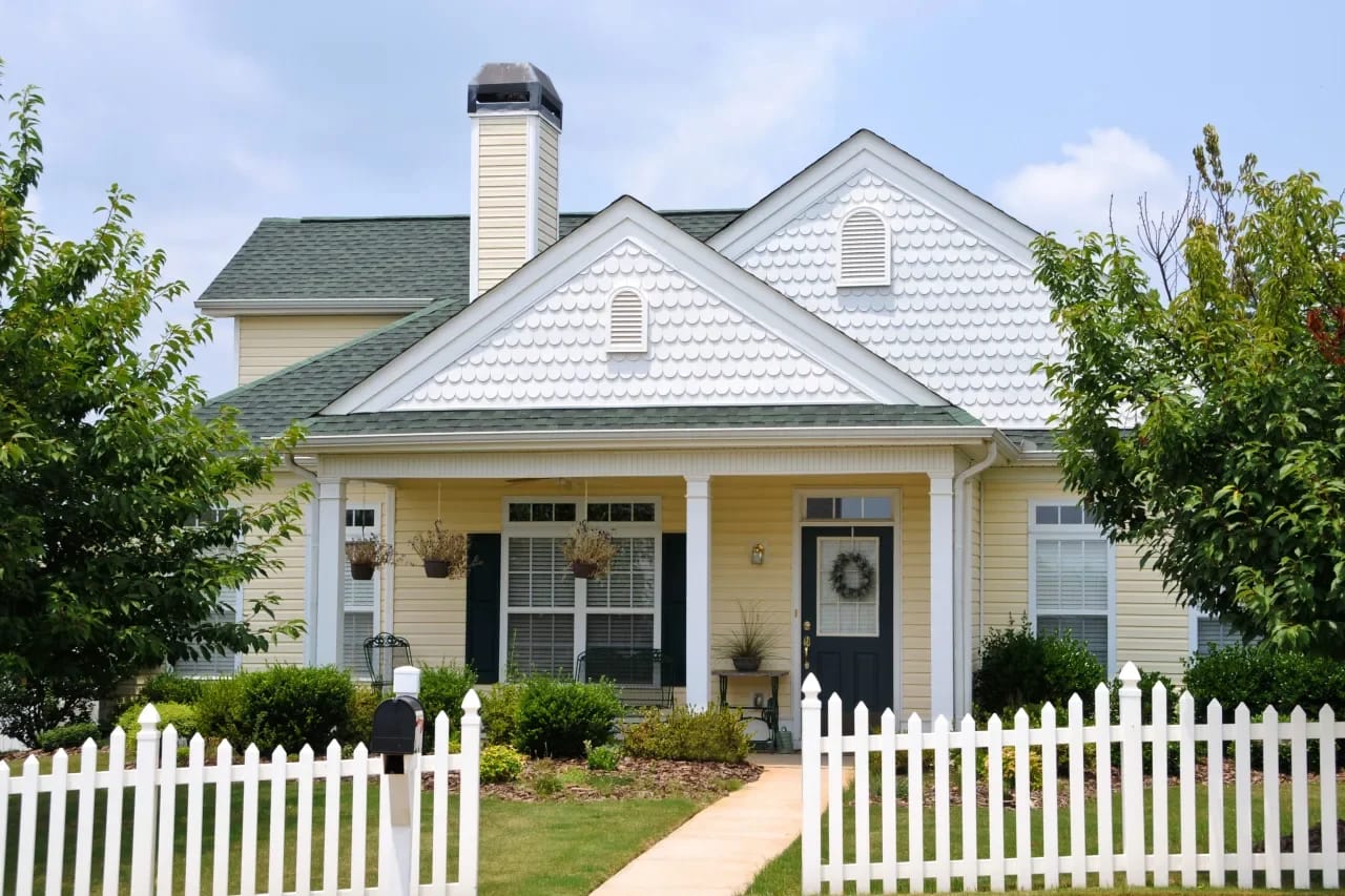 Quaint suburban home with a white picket fence and welcoming porch, embodying classic, comfortable living.