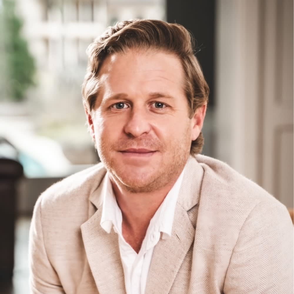 Brett Seder, a real estate professional from The Mike Seder Group, in a suit sitting at a table.