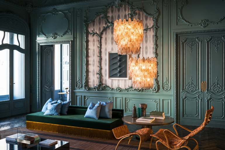 Ornate living room with teal paneled walls, amber chandeliers, and a green velvet sofa.