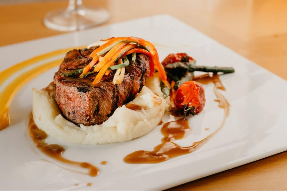 Evvia gourmet steak sitting on mashed potatoes and topped with finely chopped grilled vegetables