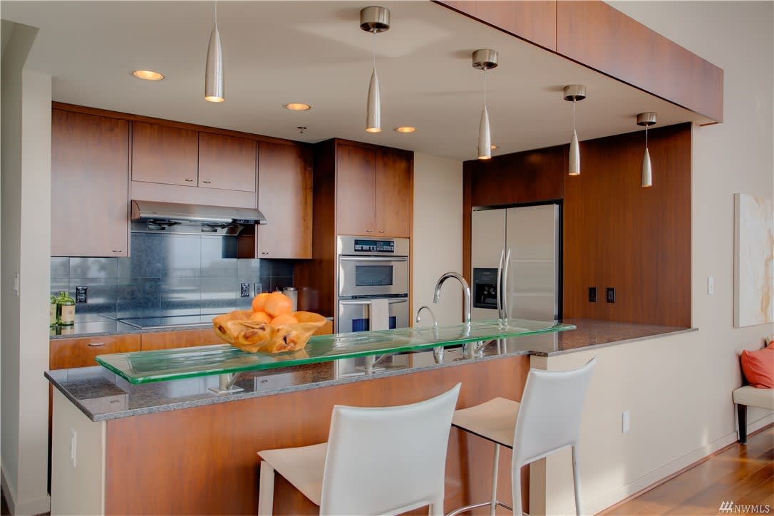 Modern kitchen with sleek wooden cabinetry, stainless steel appliances, and a glass breakfast bar.