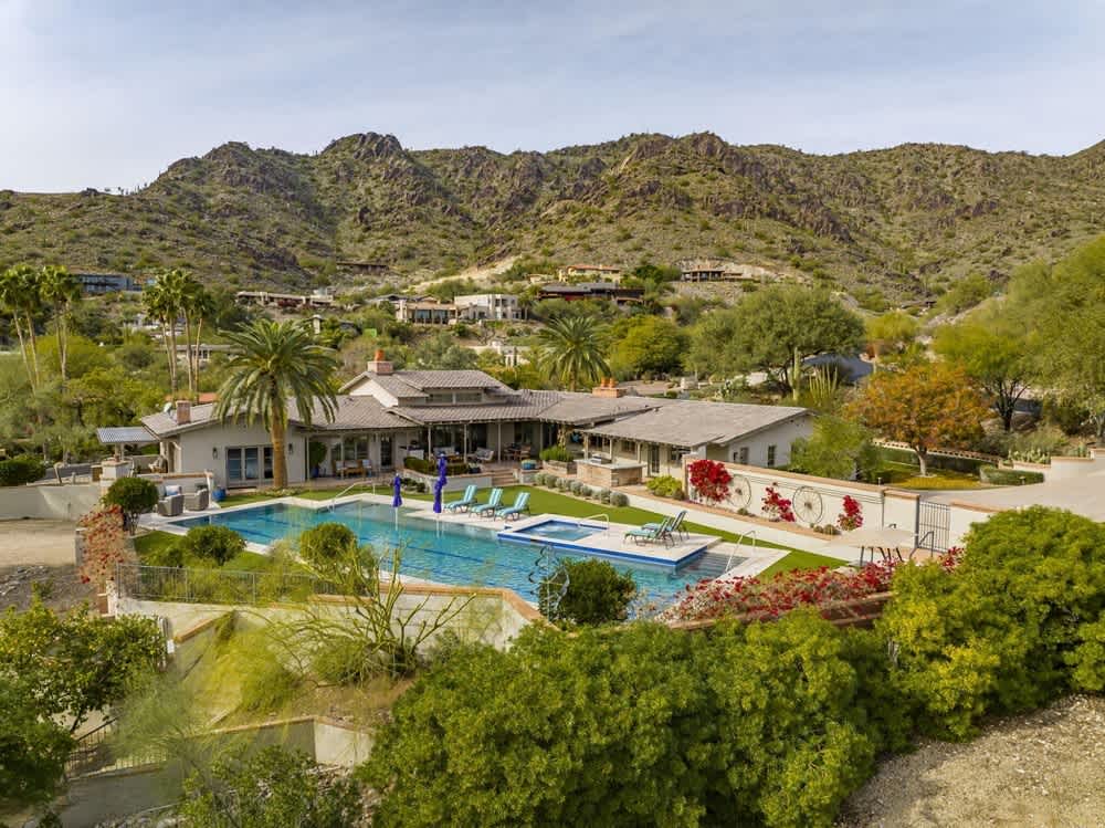 Spacious hillside property with a large swimming pool, palm trees, and a mountainous backdrop.