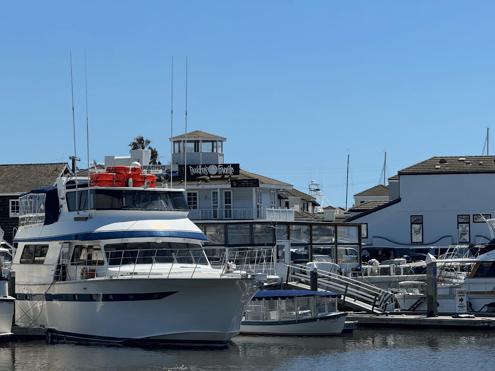 Large yacht docked at Newport Beach marina with Buddha's Favorite sushi restaurant in the background.
