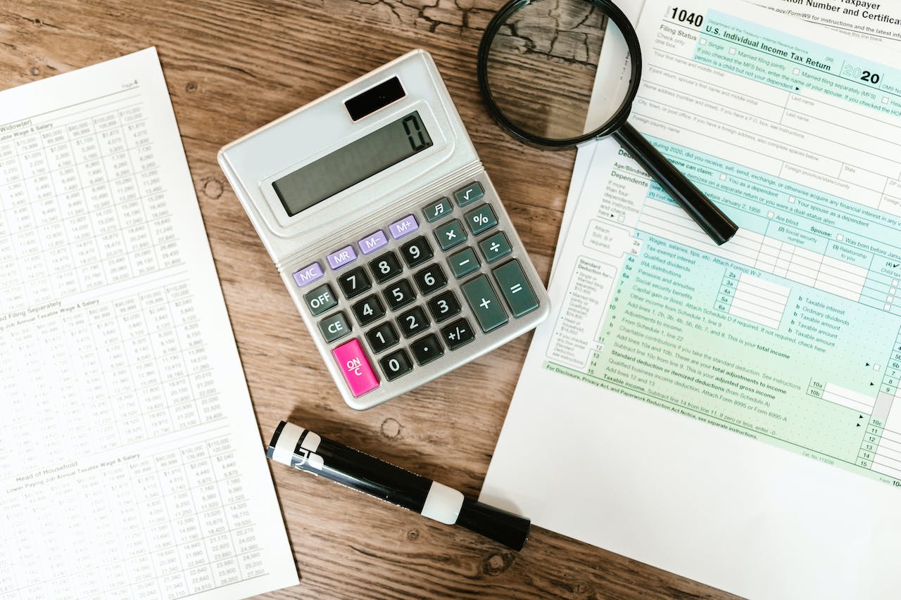 Gray calculator and black magnifying glass on a brown wooden surface.