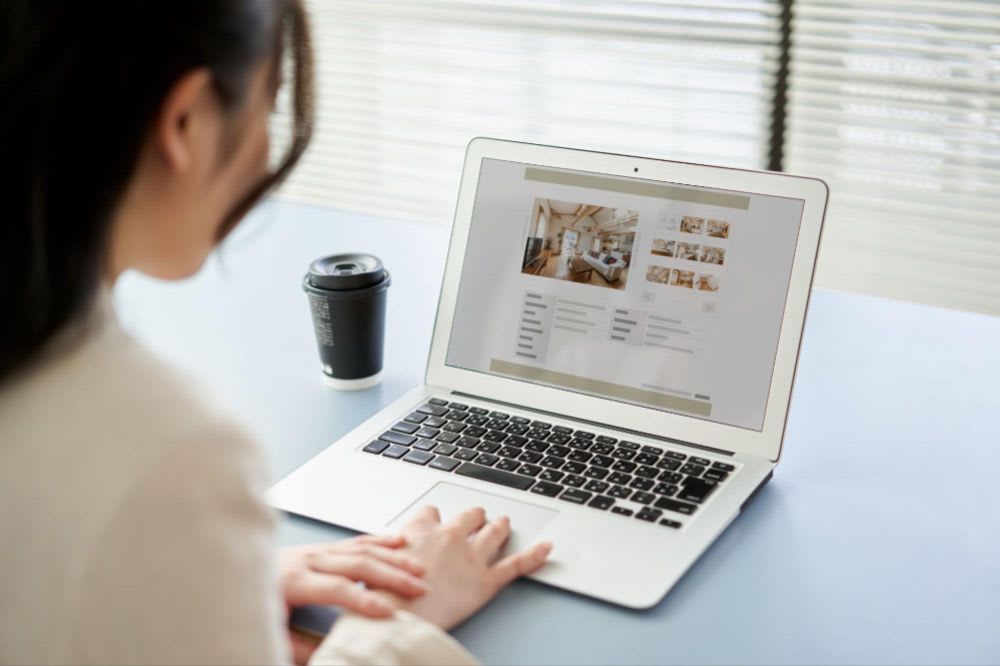 Person working on a laptop with a website displayed on the screen, alongside a coffee cup on a desk.