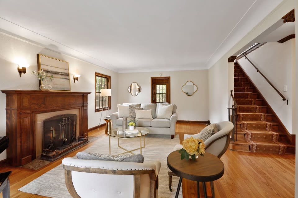 A cozy living room with a fireplace, couch, chairs, and stairs.