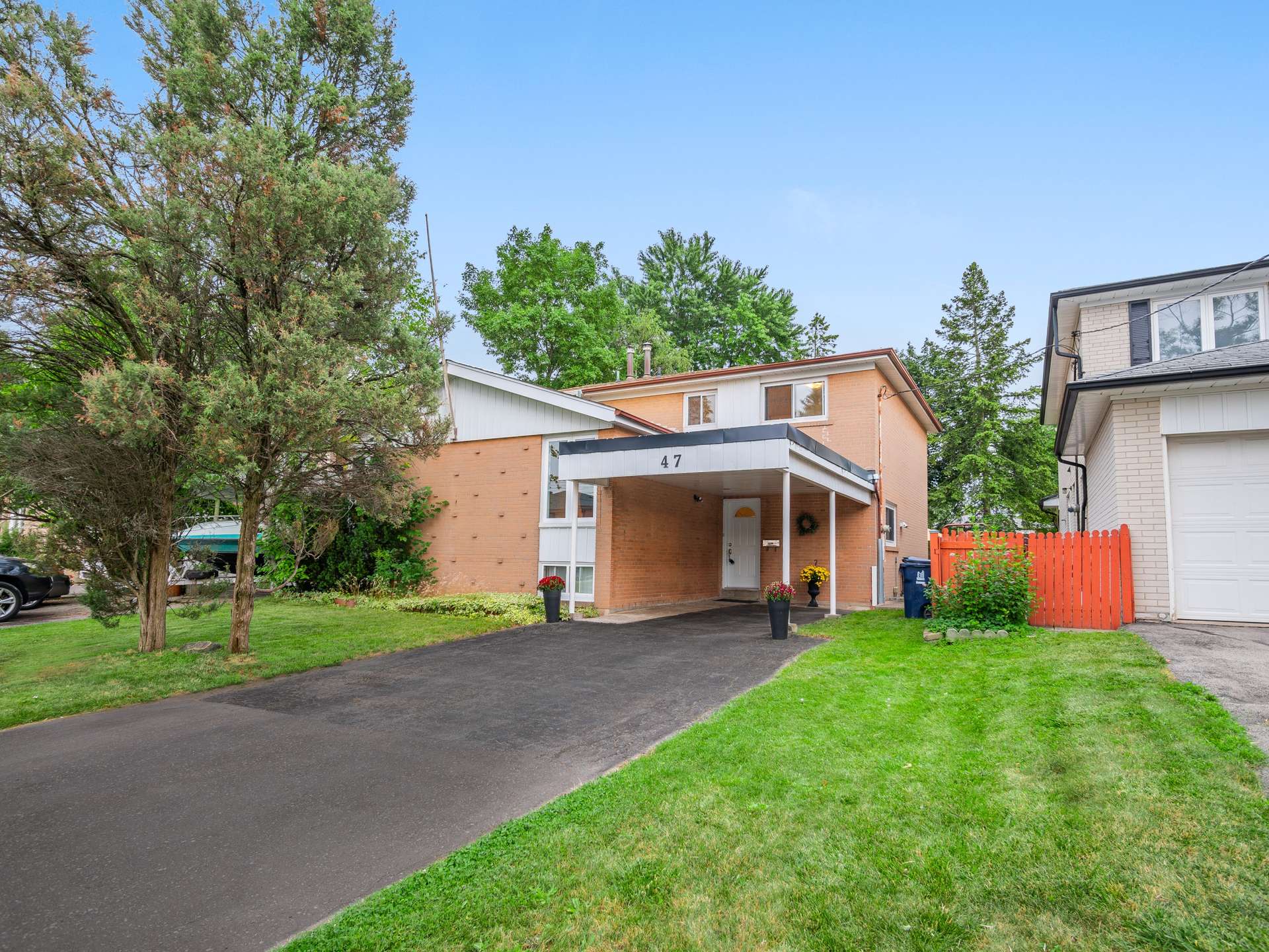 Two-story brick home with a covered entrance, paved driveway, mature trees, and front lawn.