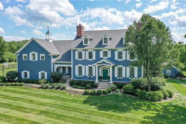 aerial view of a large, blue home, with a manicured lawn and pleasant landscaping