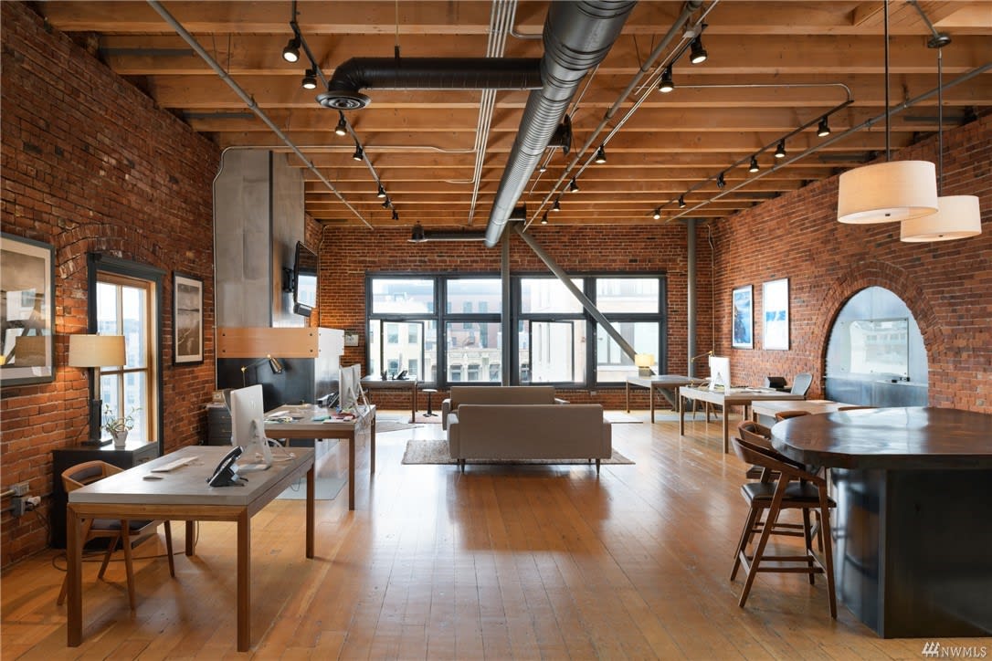 Spacious loft with exposed brick, wooden beams, and large windows, reflecting a luxurious, creative lifestyle.