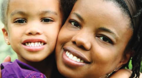Smiling woman and young child pressed cheek to cheek; the child wears purple.