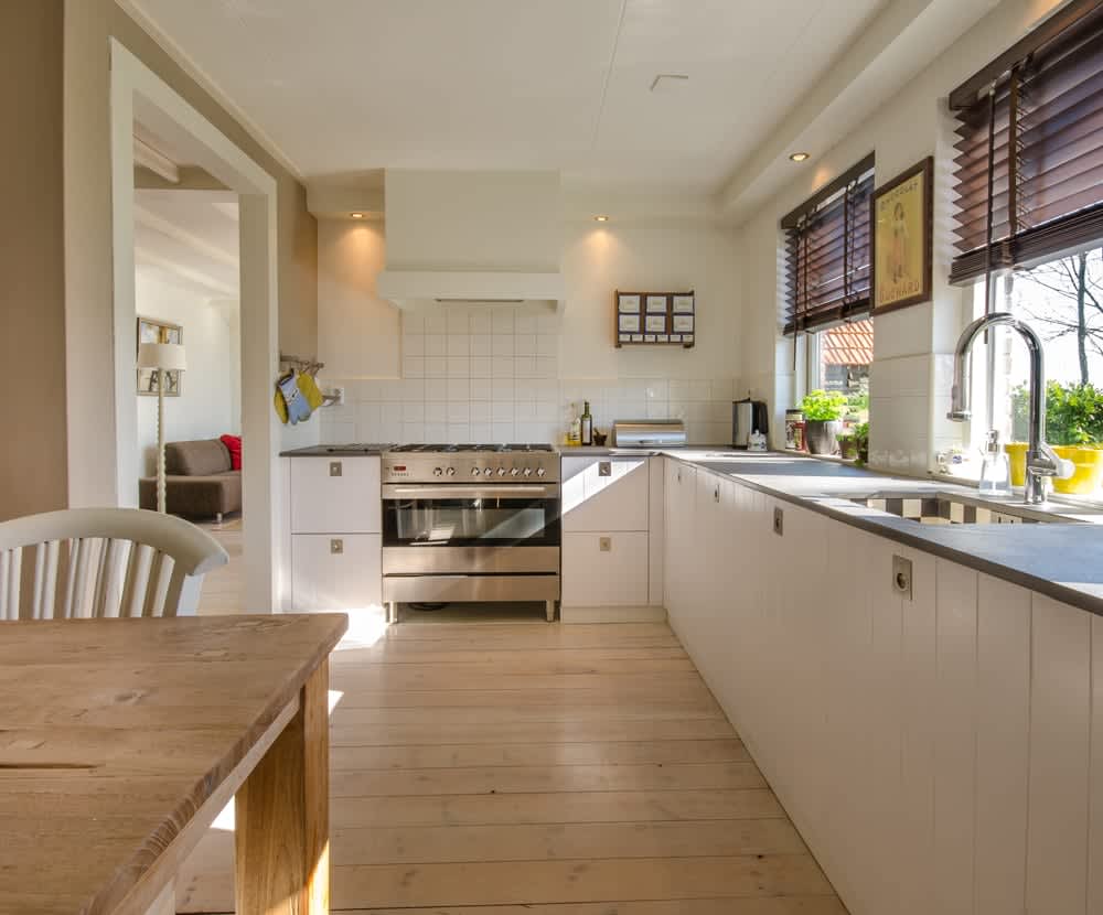 Bright kitchen with white cabinets, stainless steel range, pale wood floors, and a wooden dining table.