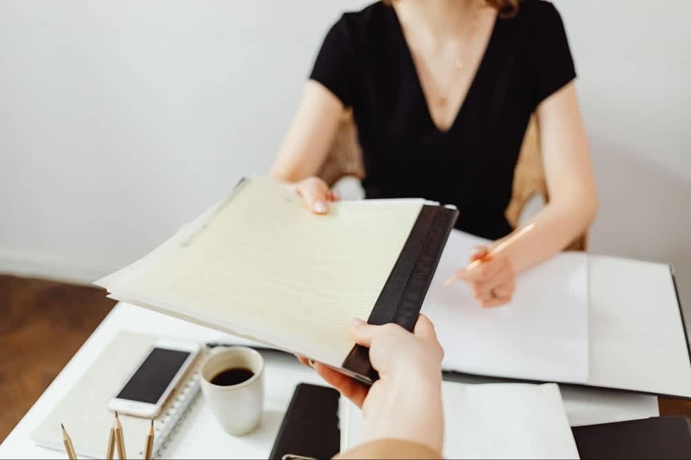 Two people review paperwork across a desk, with a coffee cup and phone nearby.