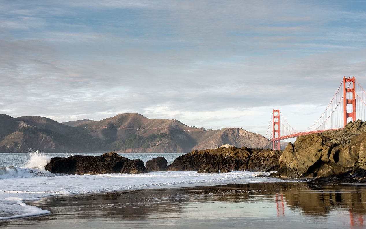 San Francisco Golden Gate Bridge viewed from Baker Beach with the Pacific Ocean surf and waves crashing on rocks