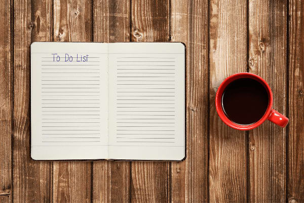 An overhead view of a cup of black coffee next to a journal open to a blank page headed by the words "To Do"