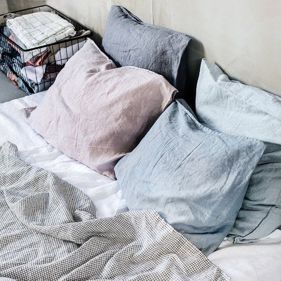 Bed layered with pale linen pillows and a wire basket of folded bedding.