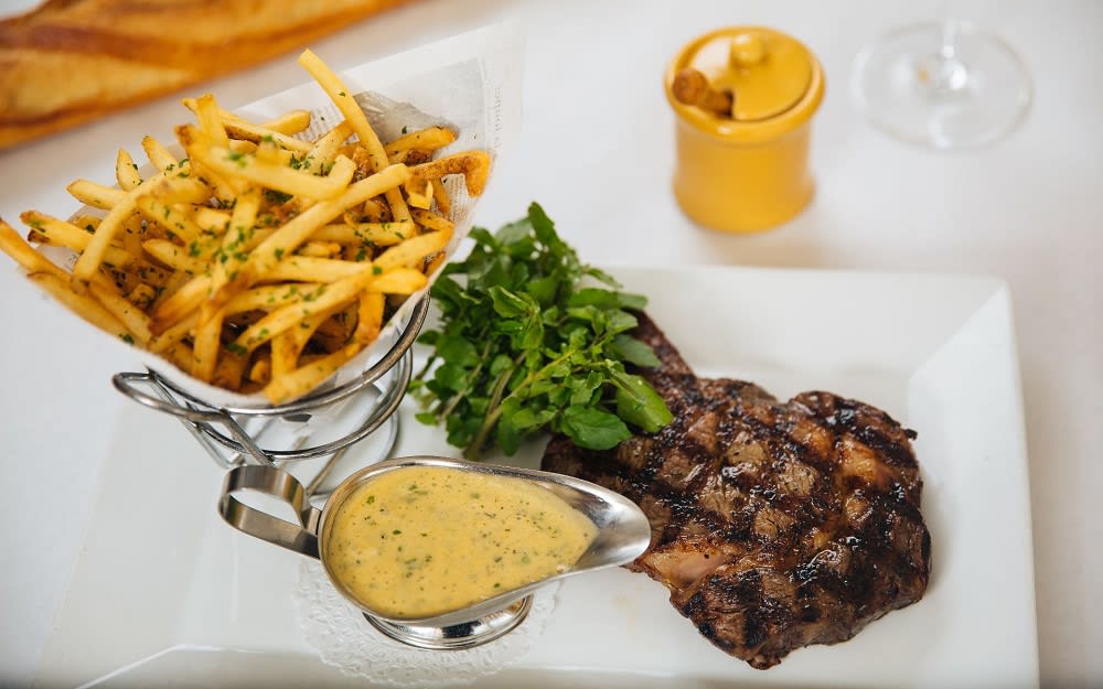 Grilled steak served with a side of herb-seasoned fries, watercress, and bearnaise sauce on a white plate.