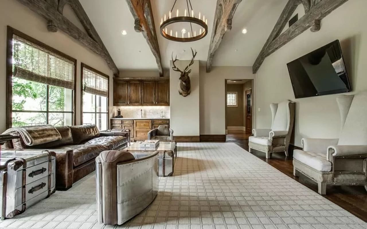 Refined rustic farmhouse-style upstairs living room featuring exposed wood beams and a tasteful animal head mounted on wall.