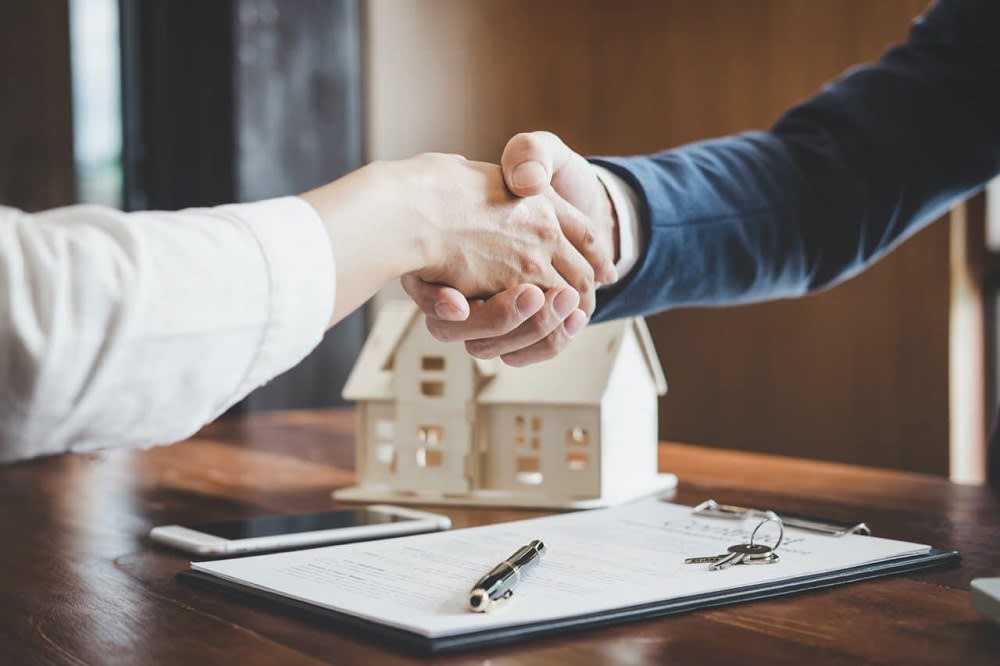 realtor handshake over a contract with keys in front of a model house