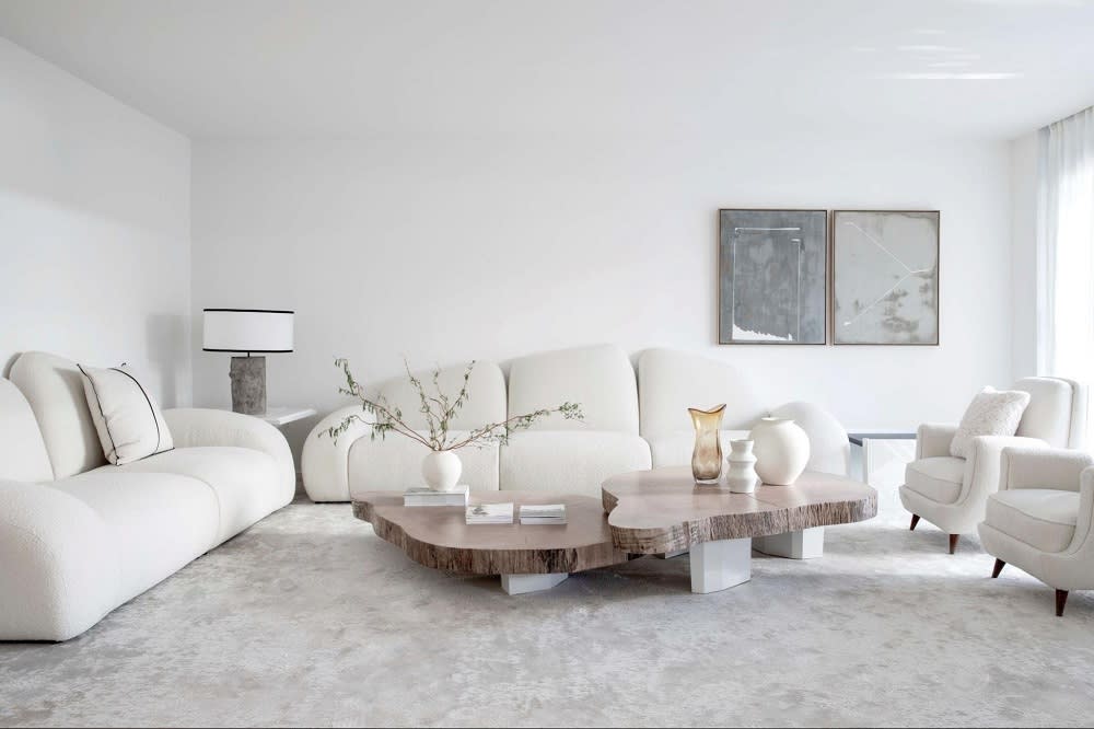 A modern living room featuring white, plush sofas, a unique wooden coffee table, and minimalist decor with soft lighting.