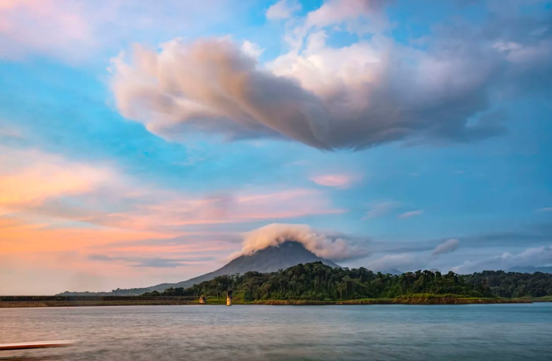 The sky is ablaze with orange, pink, and purple hues, reflecting on the water’s surface. The atmosphere is majestic.