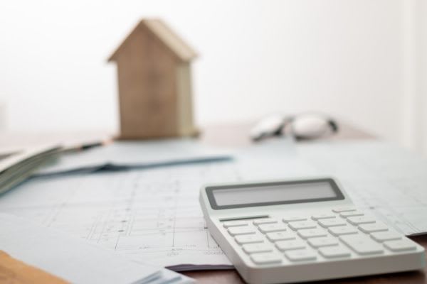 A tabletop with a calculator, paperwork, and a model of a house