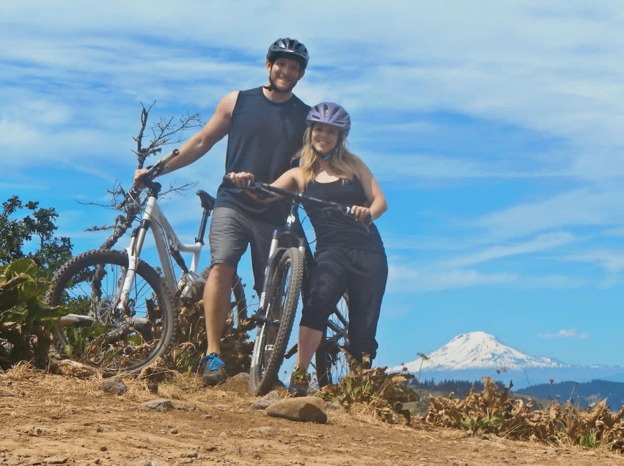 Chrissy and Brock Wood pose with mountain bikes beneath a blue sky.