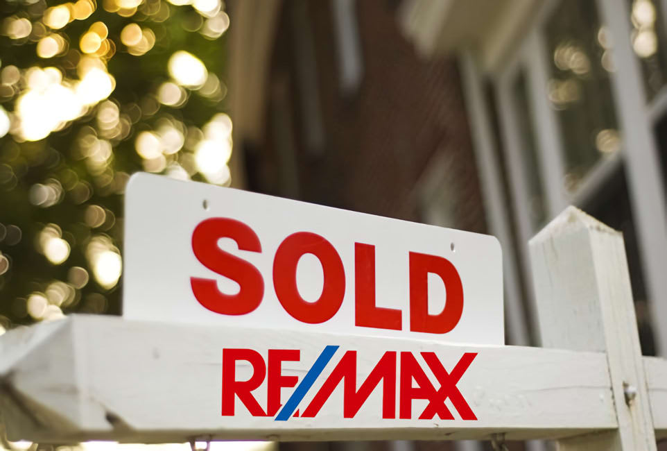 RE/MAX 'Sold' sign in front of a house, with blurred background.