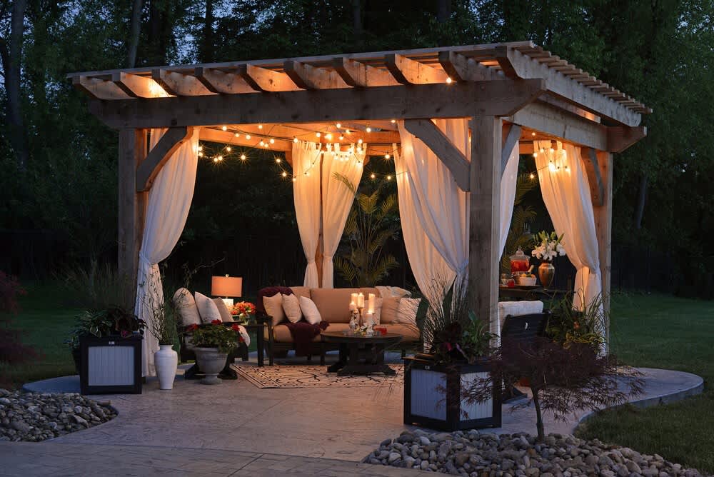 Outdoor living area with a timber pergola, white curtains, string lights, and patio seating.