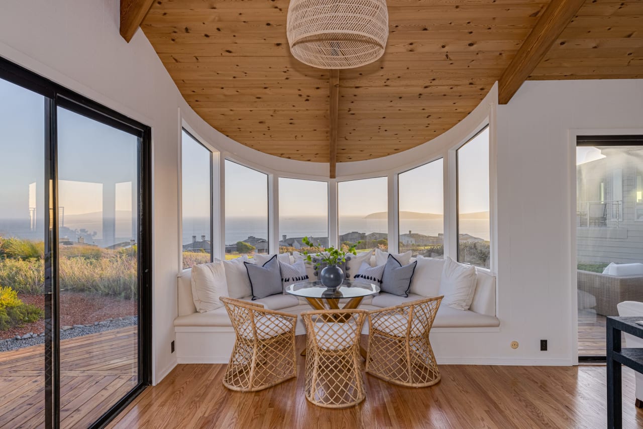 Ocean-view dining nook with curved banquette, wicker chairs, and vaulted wood ceiling.