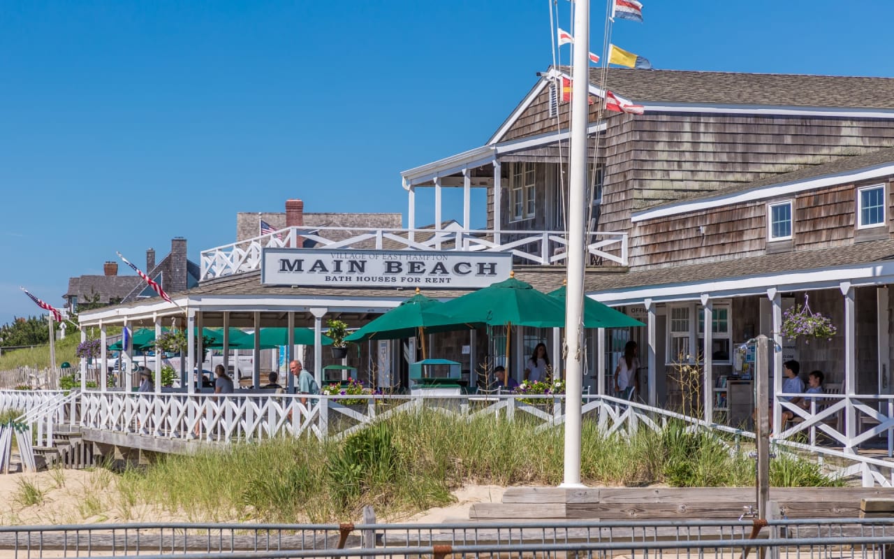 A restaurant on the beach with umbrellas and people sitting on the patio