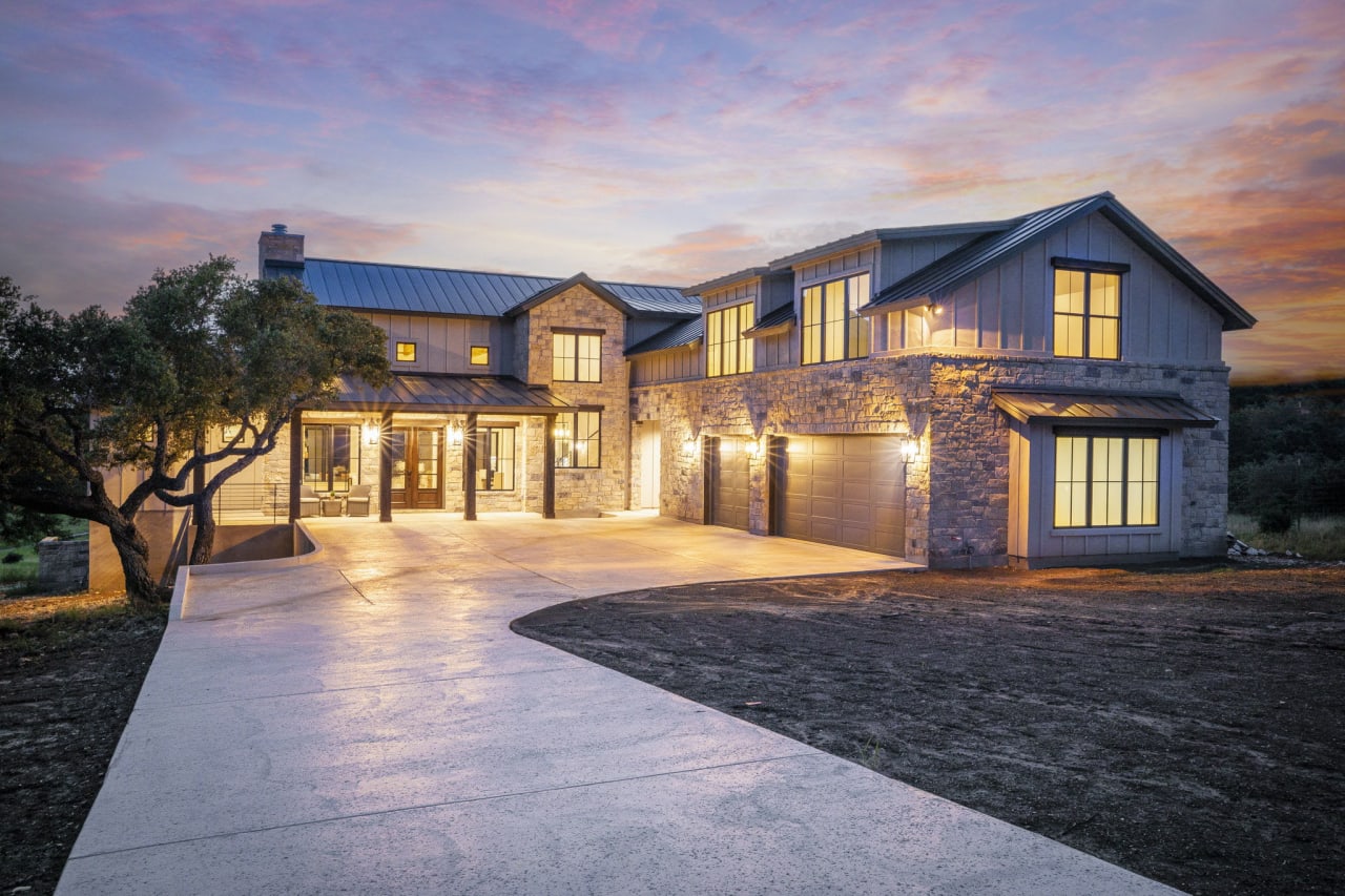 A large house with a a long concrete driveway leading up to it and with a sunset in the background.