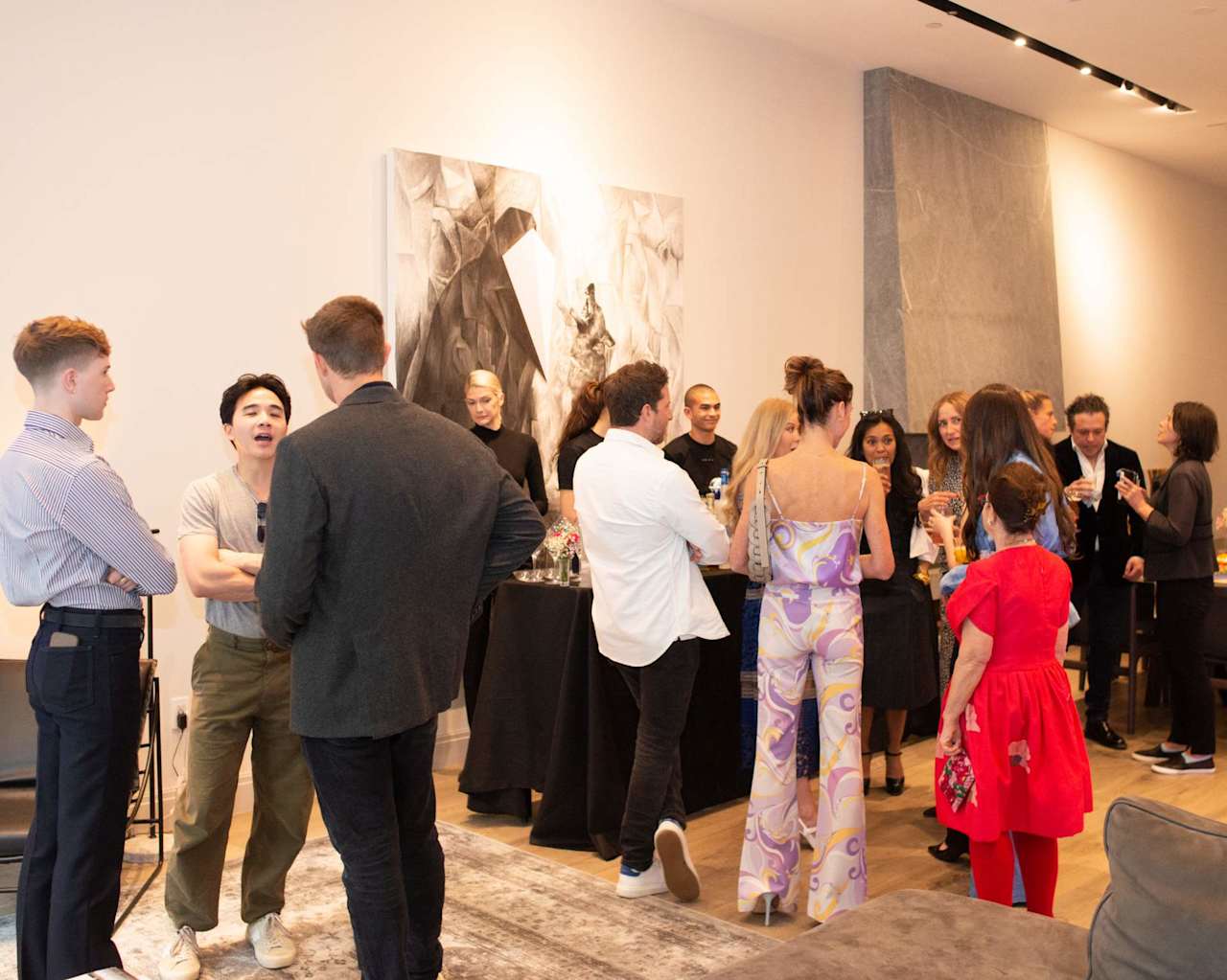 Guests mingle at an art-filled gathering, with refreshments and large abstract paintings on the walls.