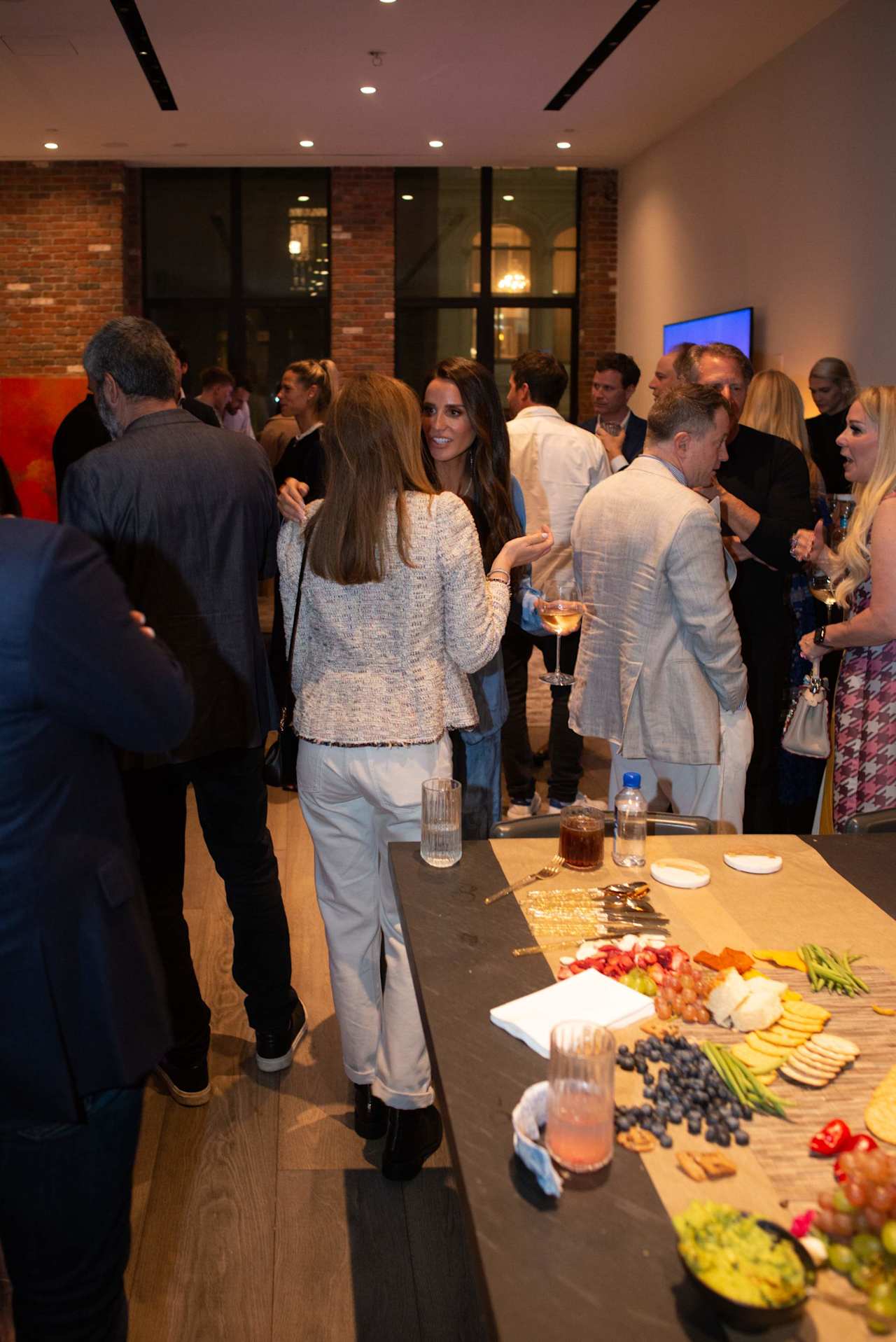 Guests mingle at an indoor event beside a buffet table with drinks and appetizers.