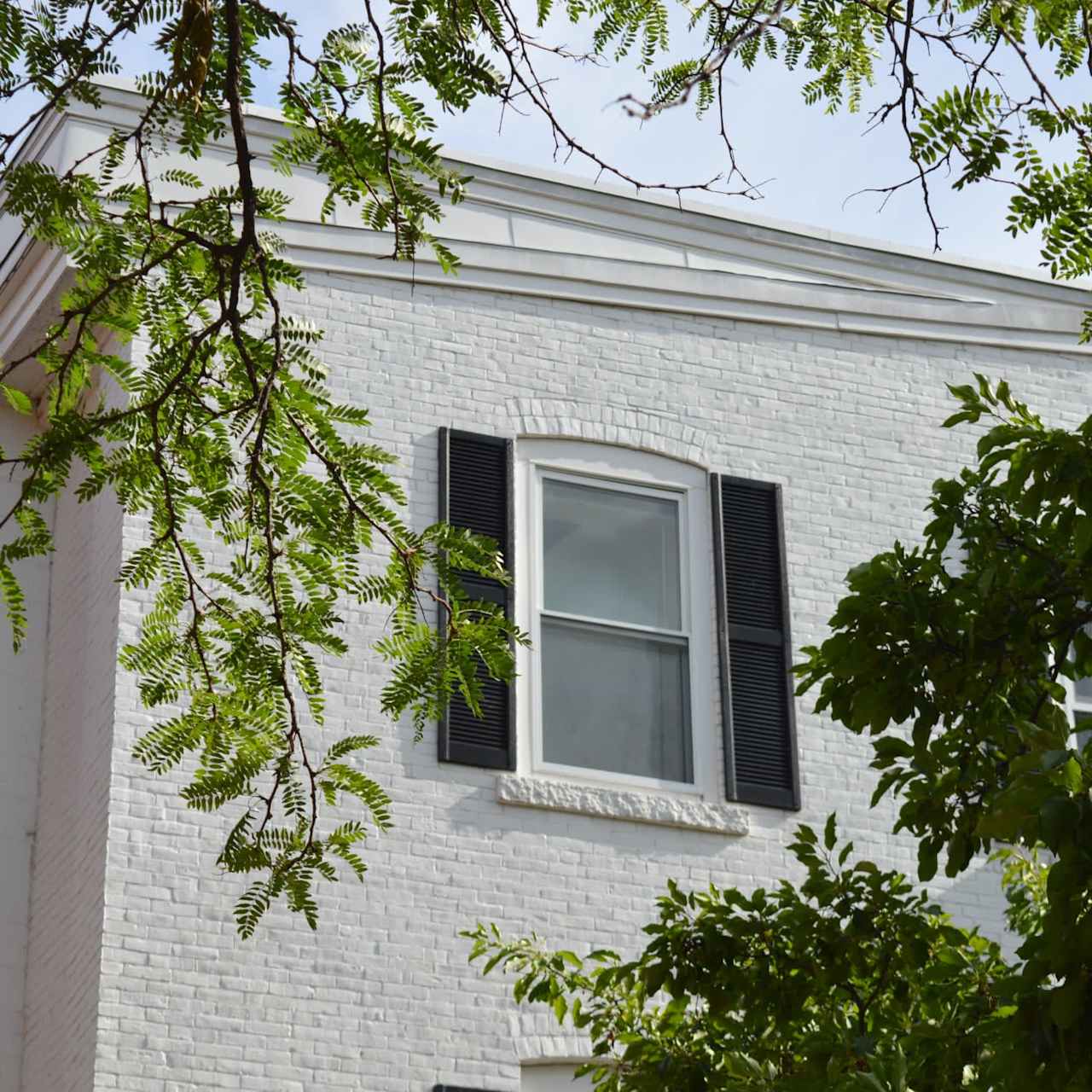 White brick home with black shutters, exuding a charming and inviting atmosphere. Ideal for families for a peaceful retreat.