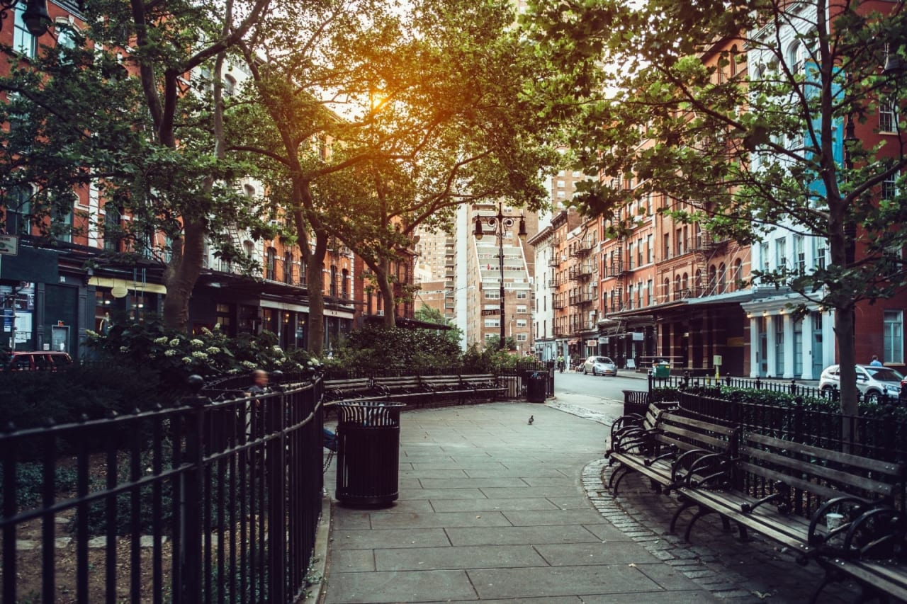 Quiet urban park with benches, trees, and historic brick buildings at sunset in a city setting.