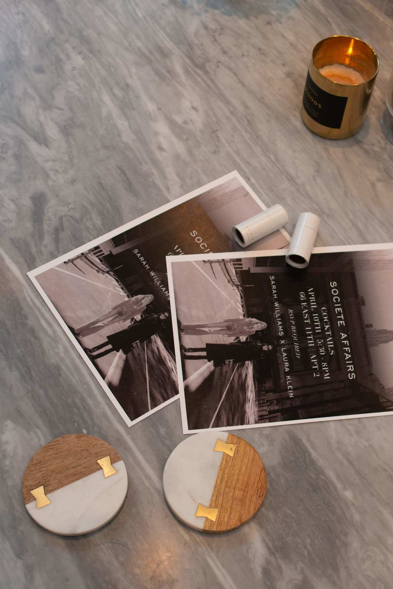 Societe Affairs cocktail event flyers on a marble surface with a gold candle and wood-and-marble coasters.