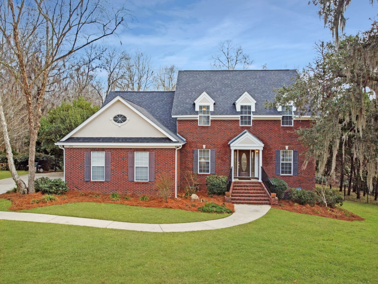 A front view of a two-story brick house with a well-maintained lawn and a pathway leading to the entrance.