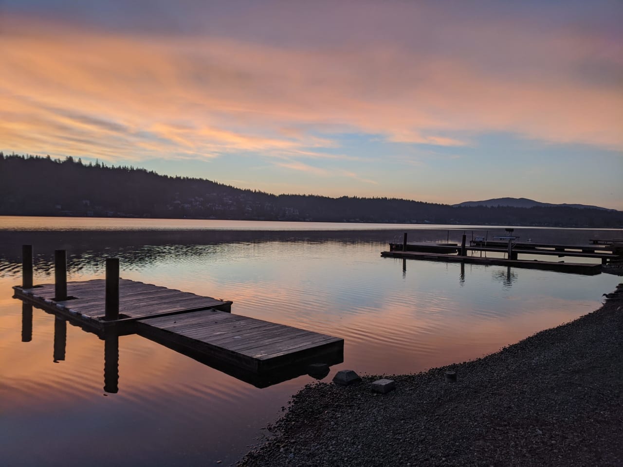 a wooden dock in the middle of a lake at sunset