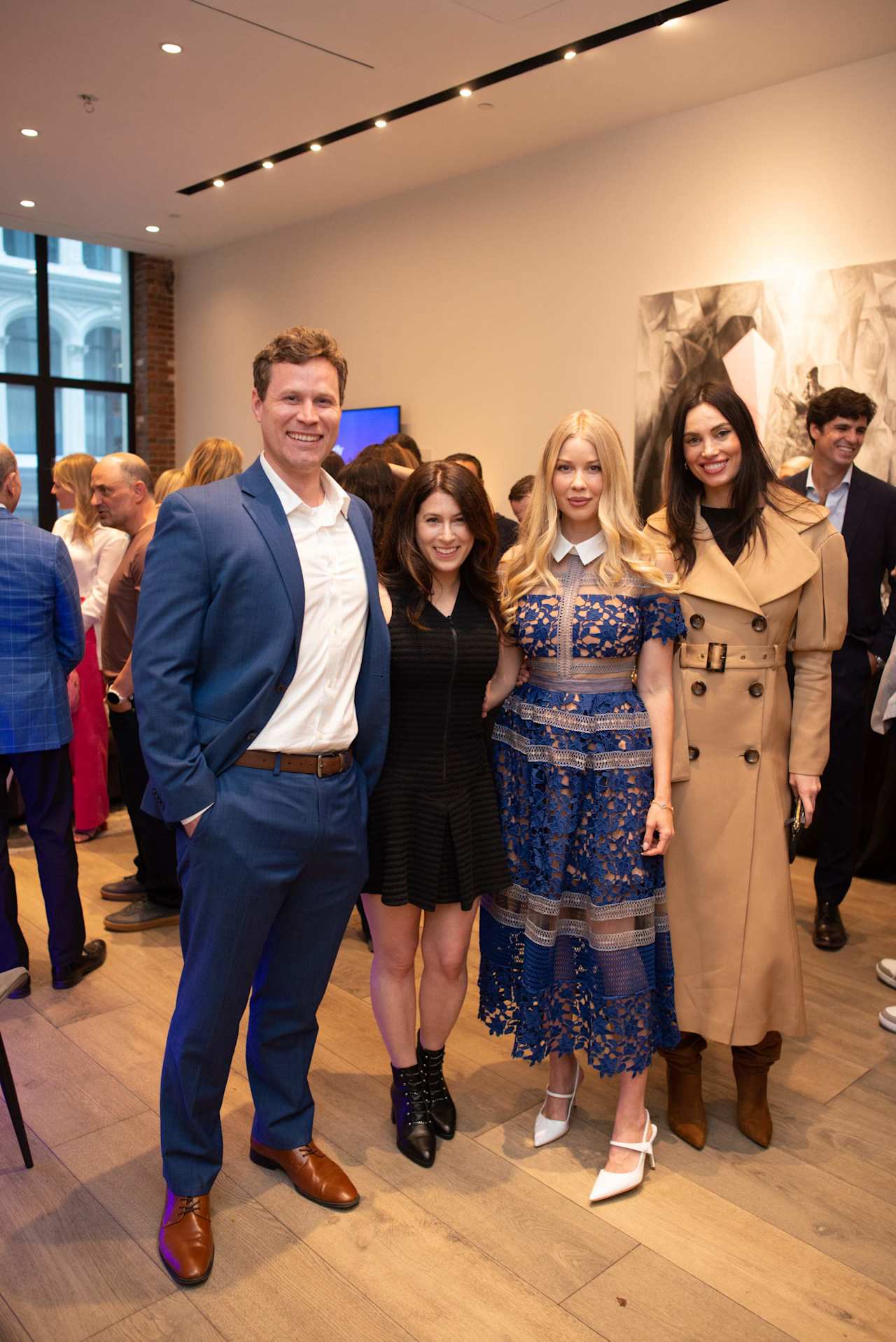 Four people pose together at an indoor event surrounded by a crowd.