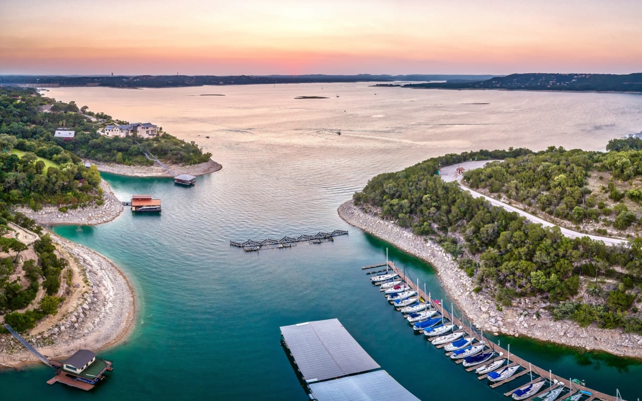Aerial view of Lake Travis at sunset, with boats docked at a marina on the right side
