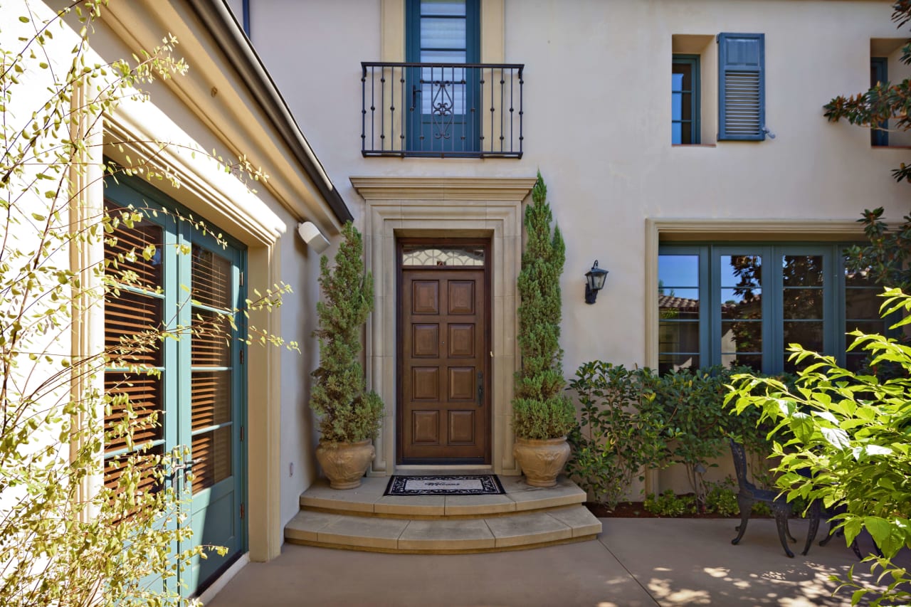 A two-story house with a white stucco exterior, a wooden door, and a balcony above it with wrought iron railings.