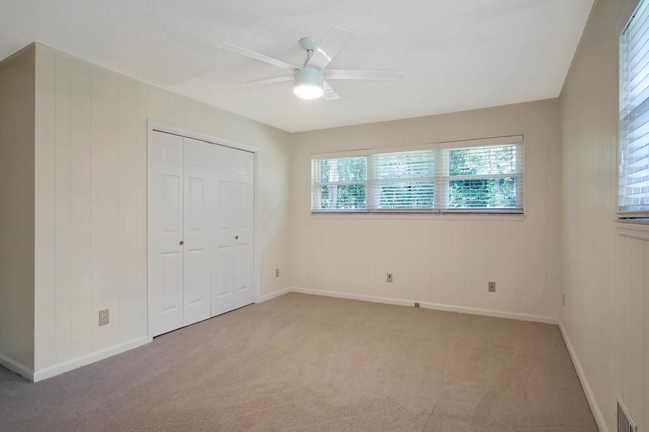 Photo of bedroom featuring a row of windows, double closet doors, lightly colored carpet,