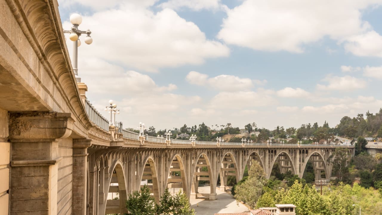 A long, curved bridge with multiple arches spanning a wide road. The bridge has a stone structure.