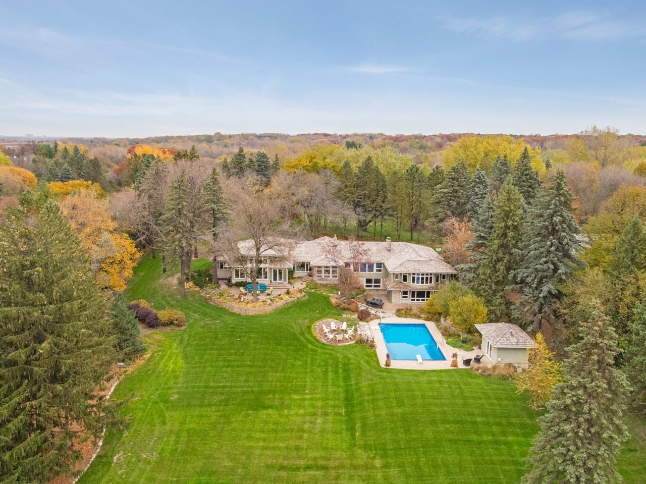 An aerial view of a large two-story house with a swimming pool, a patio, and a huge lush green yard.