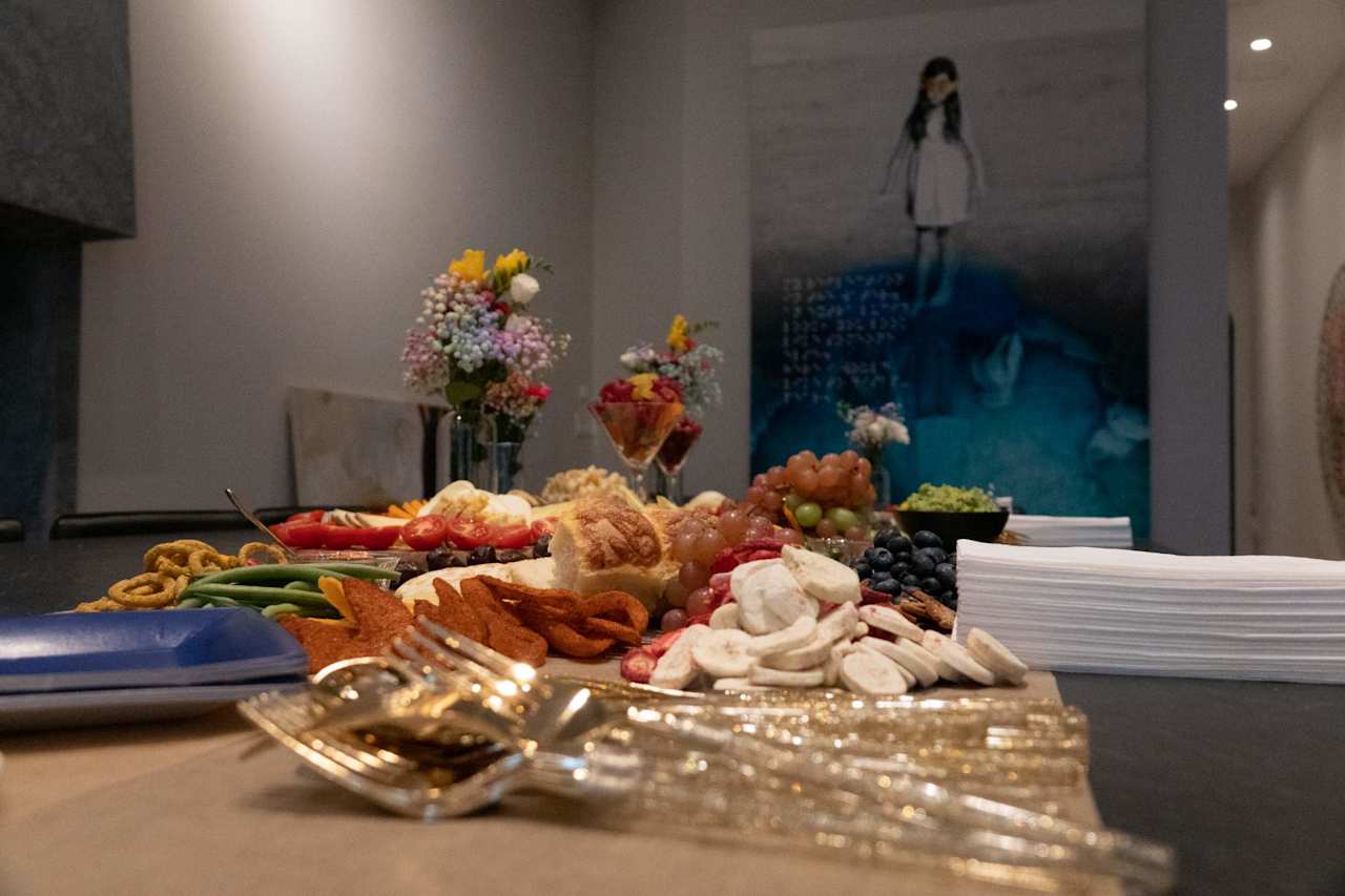 Reception buffet with appetizers, fruit, flowers, and a large blue-toned artwork behind it.