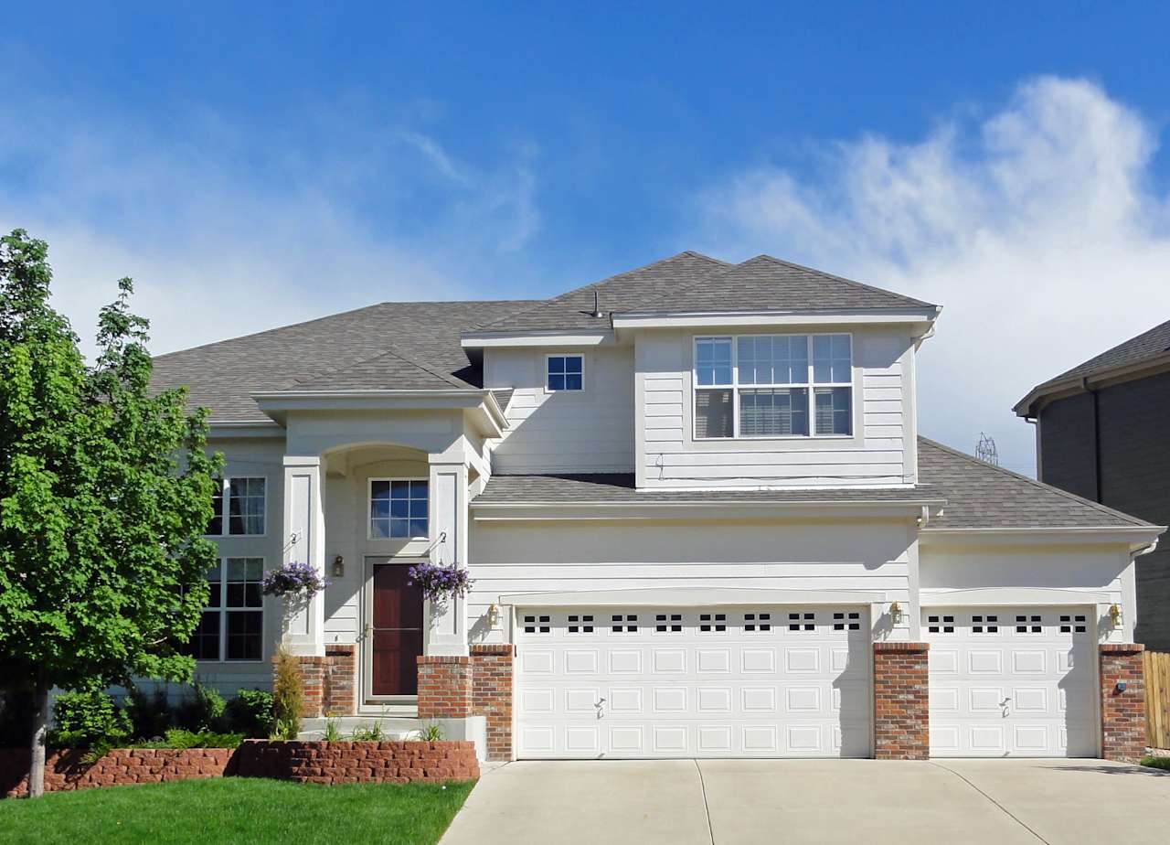 A white house with a gray roof, two garage doors, and a driveway in front of it