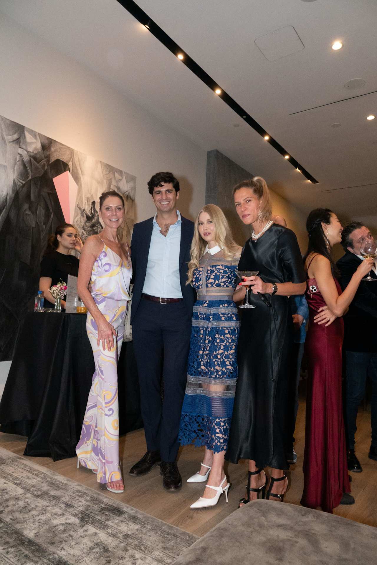 Seven adults in formal attire gather at an indoor event beside abstract wall art.