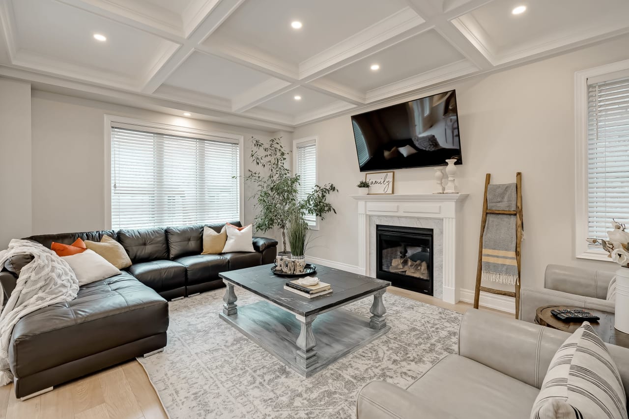 A living room with a sectional couch, two chairs, a coffee table, a fireplace, and a flat-screen TV mounted on the wall.