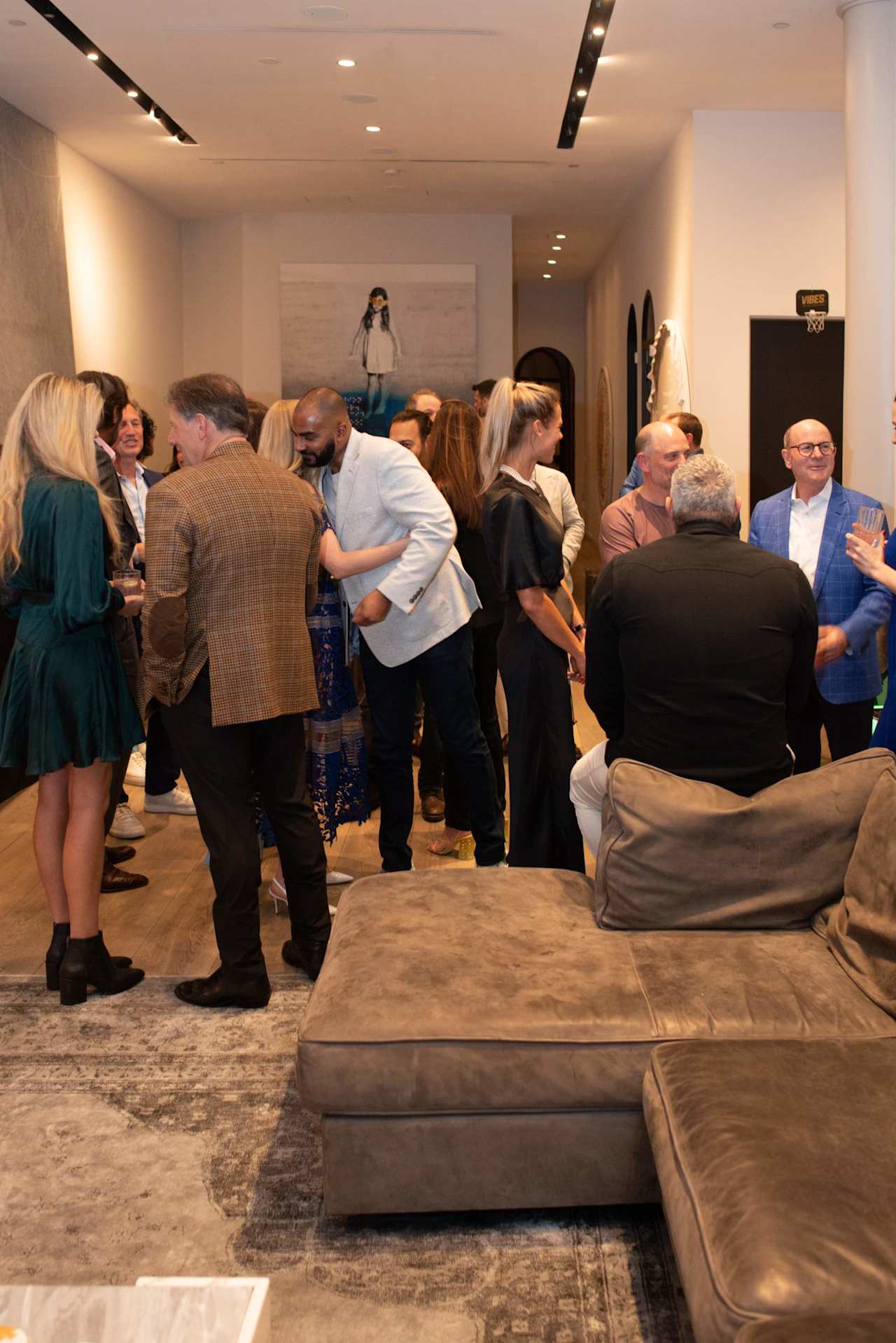 Guests mingle at a real estate event in a modern lounge with artwork and sectional seating.