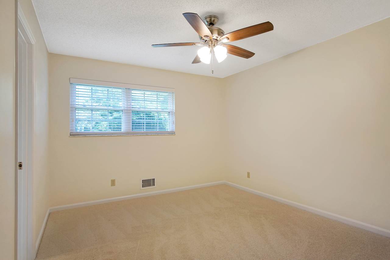 Photo of bedroom featuring lightly colored carpet, a dark wood ceiling fan and light fixture,